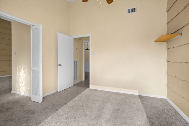 unfurnished bedroom with ceiling fan, a towering ceiling, and carpet flooring