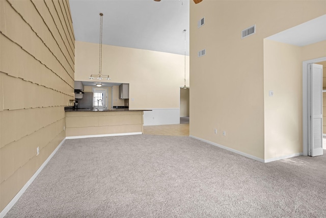 unfurnished living room featuring sink, light carpet, a towering ceiling, and ceiling fan