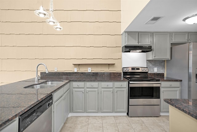 kitchen featuring hanging light fixtures, sink, light tile patterned floors, dark stone counters, and appliances with stainless steel finishes