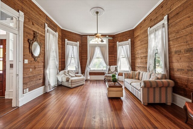 unfurnished living room featuring crown molding, dark hardwood / wood-style floors, ceiling fan, and wood walls