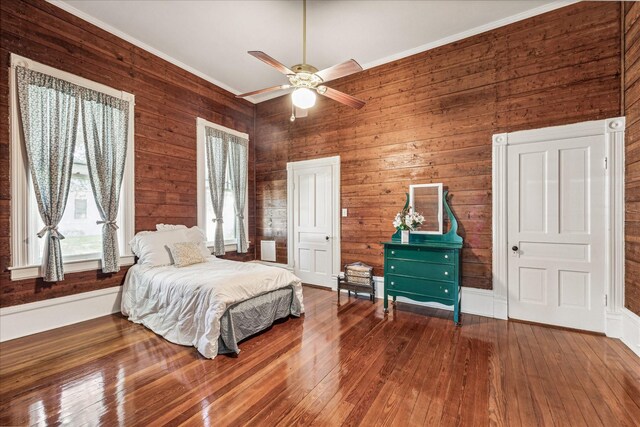 bedroom featuring ornamental molding, dark wood-type flooring, wooden walls, and ceiling fan