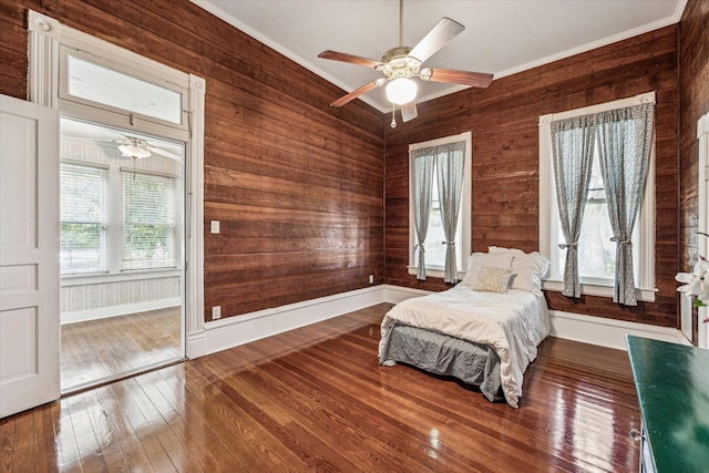 bedroom featuring wood walls, ceiling fan, crown molding, and dark wood-type flooring