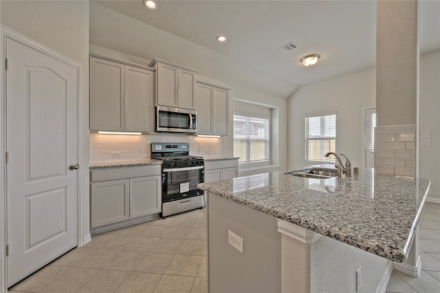 kitchen with lofted ceiling, sink, light tile patterned floors, appliances with stainless steel finishes, and light stone counters