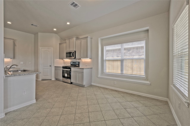 kitchen with sink, vaulted ceiling, appliances with stainless steel finishes, light tile patterned flooring, and light stone counters