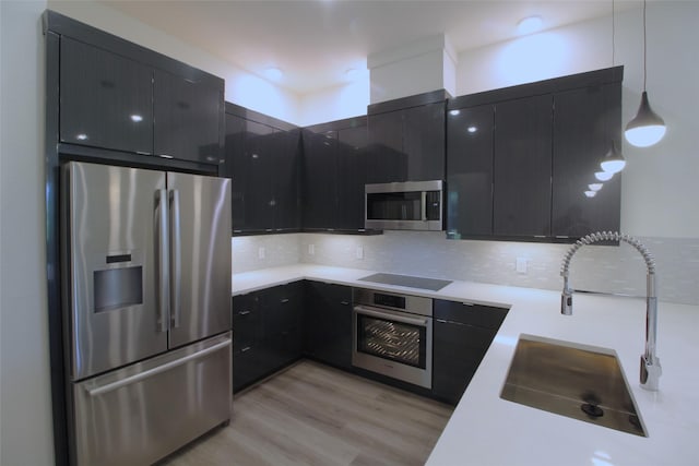 kitchen featuring stainless steel appliances, sink, hanging light fixtures, backsplash, and light wood-type flooring