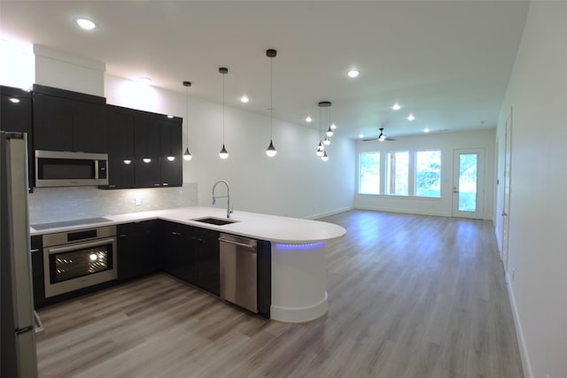 kitchen with decorative light fixtures, ceiling fan, kitchen peninsula, sink, and stainless steel appliances