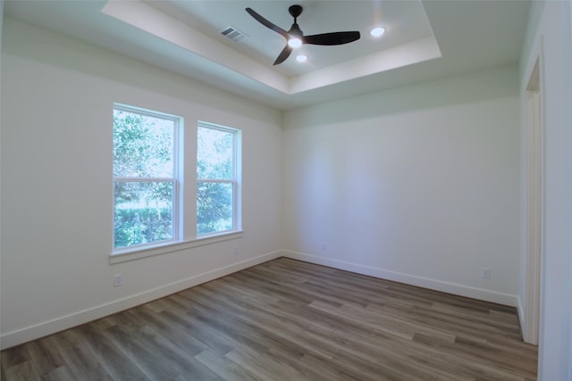 empty room with ceiling fan, hardwood / wood-style floors, and a tray ceiling