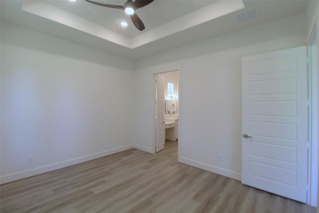 unfurnished bedroom featuring a raised ceiling, ceiling fan, connected bathroom, and light hardwood / wood-style floors