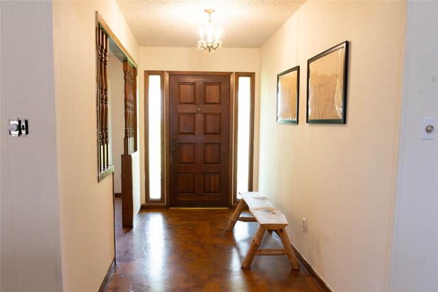 foyer entrance with dark wood-type flooring, a textured ceiling, and a notable chandelier