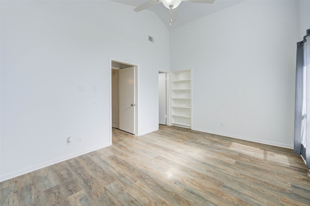 empty room with light wood-type flooring, ceiling fan, and high vaulted ceiling