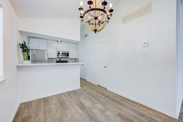 kitchen with lofted ceiling, tasteful backsplash, a chandelier, light wood-type flooring, and stainless steel appliances