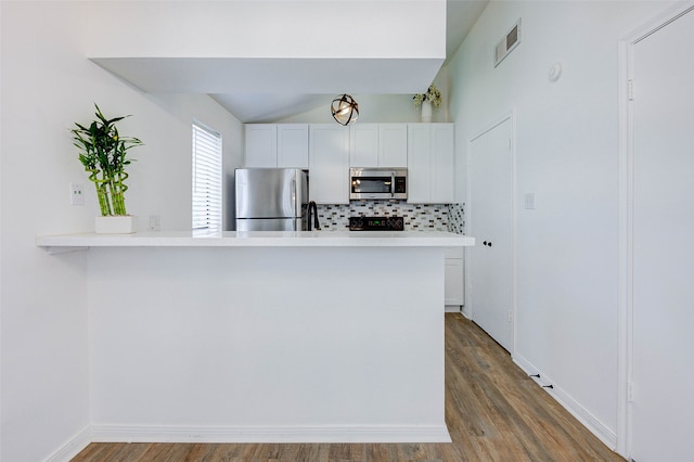 kitchen with kitchen peninsula, white cabinets, appliances with stainless steel finishes, decorative backsplash, and hardwood / wood-style flooring