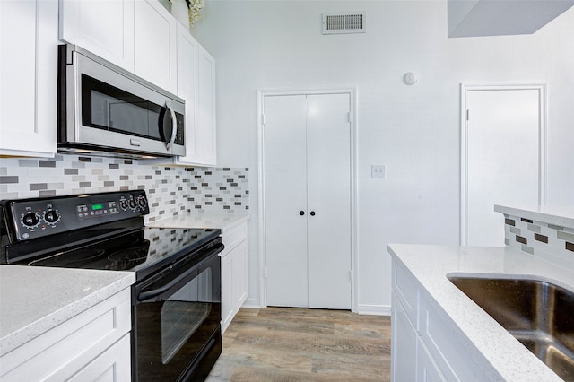 kitchen with black electric range, white cabinetry, decorative backsplash, light wood-type flooring, and light stone counters