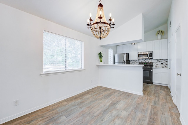 kitchen featuring stainless steel appliances, vaulted ceiling, kitchen peninsula, decorative backsplash, and light wood-type flooring