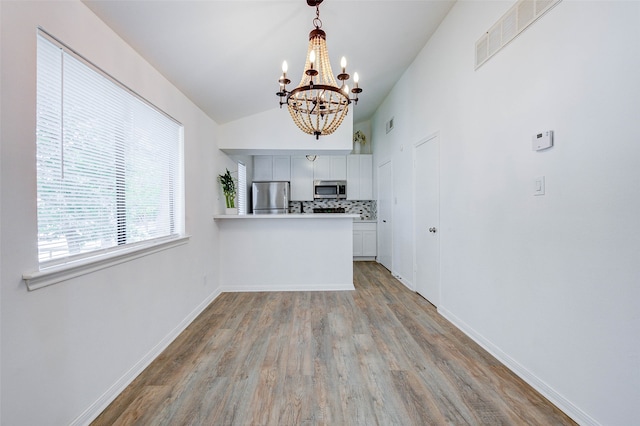 kitchen with a chandelier, decorative backsplash, appliances with stainless steel finishes, light hardwood / wood-style flooring, and kitchen peninsula