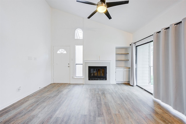 unfurnished living room with a fireplace, light wood-type flooring, ceiling fan, and a healthy amount of sunlight