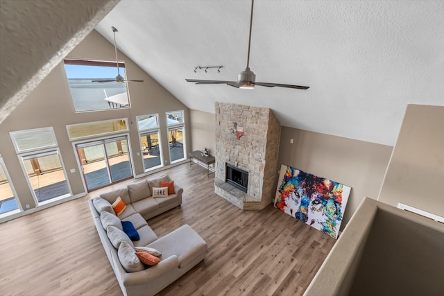 living room featuring hardwood / wood-style floors, a stone fireplace, a textured ceiling, and ceiling fan