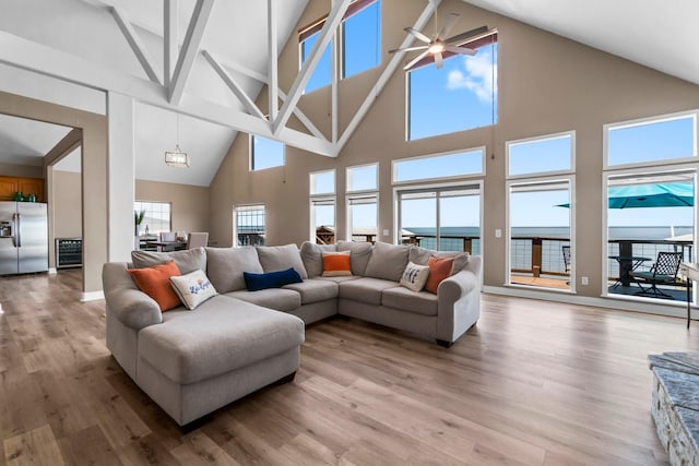 living room featuring light wood-type flooring, high vaulted ceiling, ceiling fan, and a water view