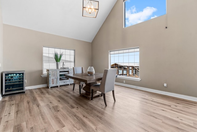 dining space featuring high vaulted ceiling, a chandelier, wine cooler, and light wood-type flooring