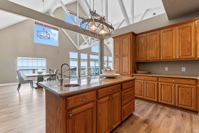 kitchen with pendant lighting, sink, a kitchen island with sink, light hardwood / wood-style floors, and an inviting chandelier