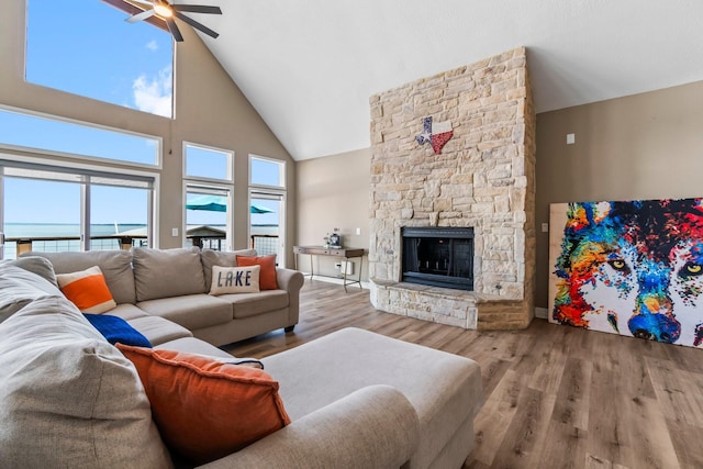 living room with ceiling fan, hardwood / wood-style floors, high vaulted ceiling, a water view, and a fireplace