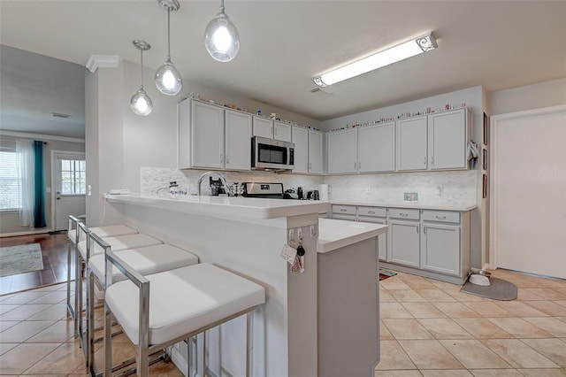 kitchen with pendant lighting, a kitchen breakfast bar, ornamental molding, appliances with stainless steel finishes, and kitchen peninsula