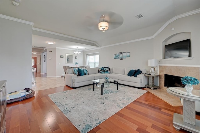 living room featuring a tile fireplace, light wood-type flooring, ceiling fan with notable chandelier, and ornamental molding