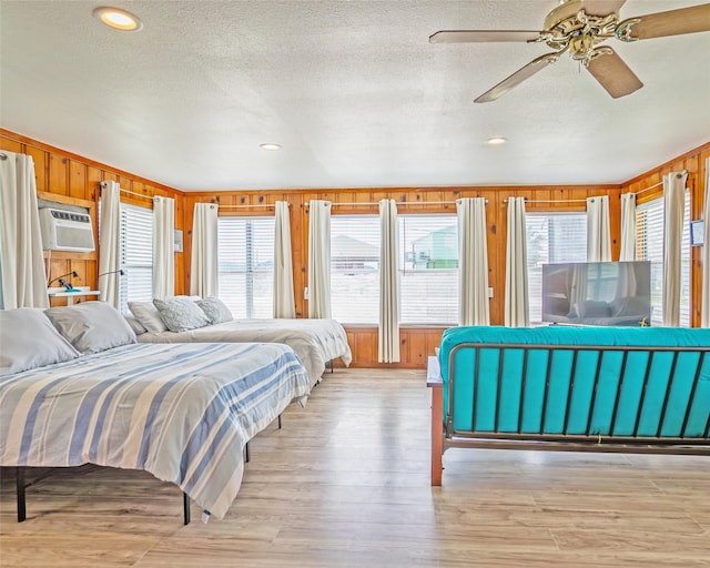 1214 County Road 201, Sargent, TX 77414 - bedroom featuring multiple windows, wooden walls, a textured ceiling, a wall mounted air conditioner, and light wood finished floors