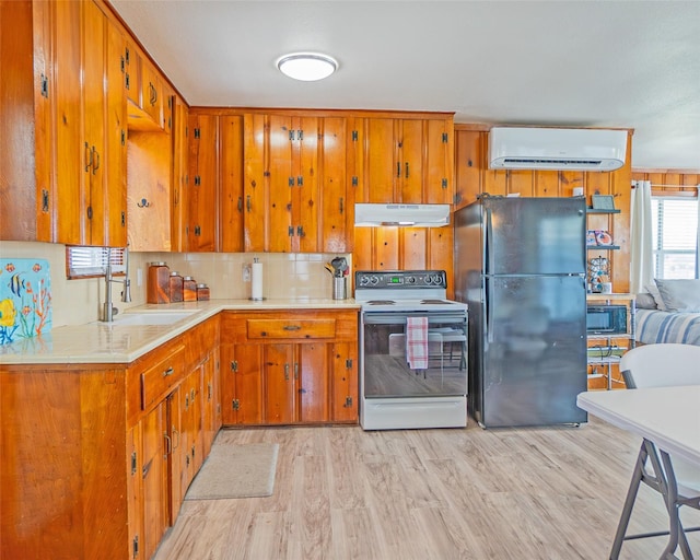 kitchen with under cabinet range hood, electric range, light countertops, freestanding refrigerator, and a wall mounted air conditioner