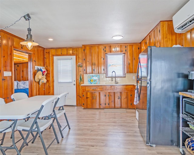 kitchen with brown cabinetry, light countertops, an AC wall unit, and freestanding refrigerator