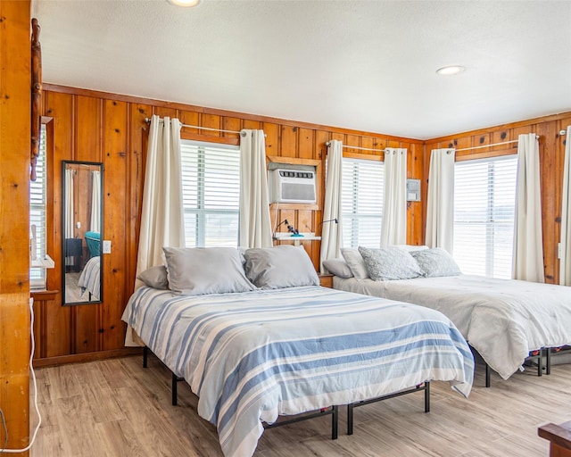 bedroom featuring wood walls, light wood-style floors, and an AC wall unit