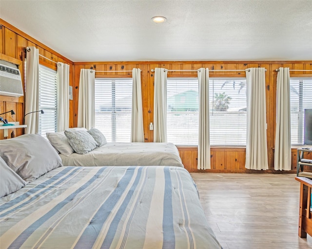 bedroom featuring a textured ceiling, wood walls, a wall mounted air conditioner, and light wood-style floors