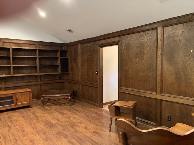 sitting room featuring wood walls, wood-type flooring, and vaulted ceiling