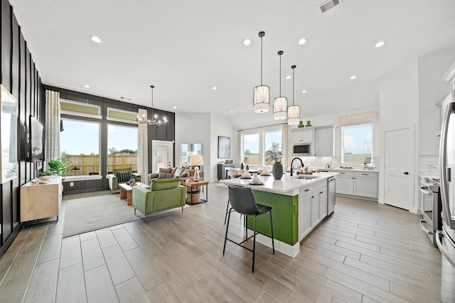 kitchen with a kitchen island with sink, sink, pendant lighting, white cabinetry, and a breakfast bar area