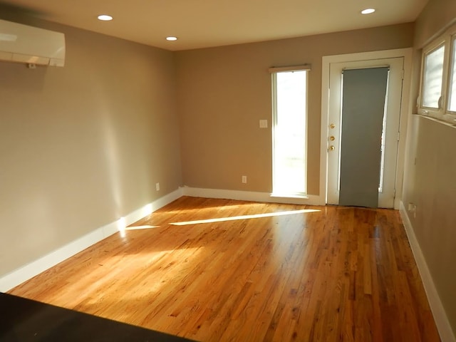 unfurnished room featuring a wealth of natural light, a wall mounted AC, and hardwood / wood-style floors