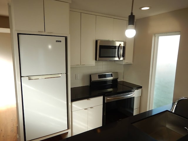 kitchen with appliances with stainless steel finishes, white cabinetry, tasteful backsplash, and pendant lighting