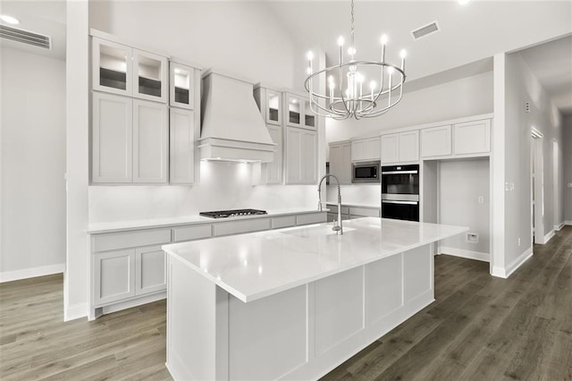 kitchen with premium range hood, a kitchen island with sink, white cabinets, sink, and appliances with stainless steel finishes