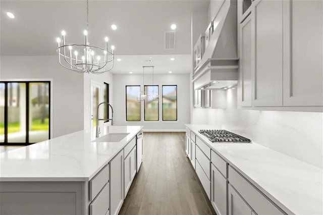 kitchen featuring light stone countertops, custom range hood, a spacious island, sink, and decorative light fixtures