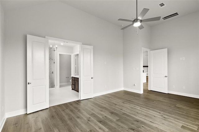 unfurnished bedroom with wood-type flooring, ceiling fan with notable chandelier, high vaulted ceiling, and ensuite bath