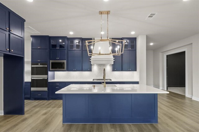 kitchen with light wood-type flooring, stainless steel appliances, blue cabinetry, and a kitchen island with sink