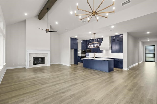 kitchen featuring premium range hood, an island with sink, decorative light fixtures, a fireplace, and beamed ceiling