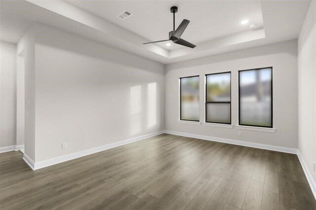 empty room with ceiling fan, dark wood-type flooring, and a raised ceiling