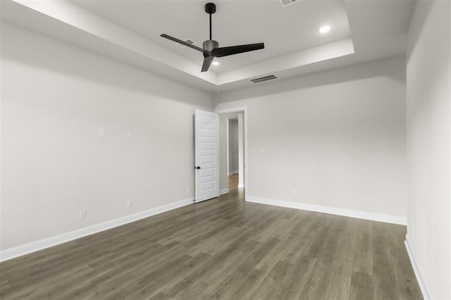 spare room featuring dark wood-type flooring, a tray ceiling, and ceiling fan