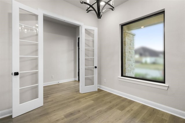 unfurnished room featuring french doors, wood-type flooring, and a notable chandelier