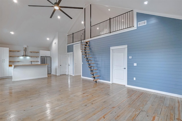 unfurnished living room featuring ceiling fan, high vaulted ceiling, wood walls, and light wood-type flooring