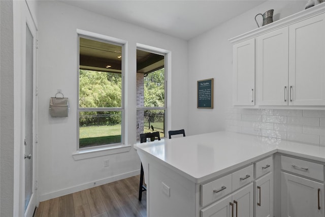 kitchen with white cabinets, light hardwood / wood-style floors, kitchen peninsula, and tasteful backsplash