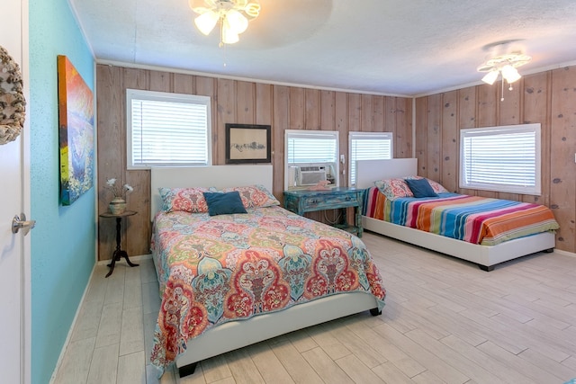 bedroom featuring ceiling fan, light hardwood / wood-style floors, cooling unit, and wood walls