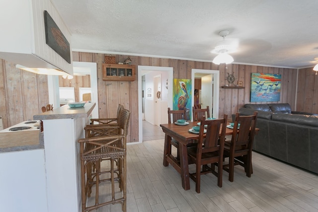 dining area featuring ceiling fan, wooden walls, a textured ceiling, and light hardwood / wood-style flooring