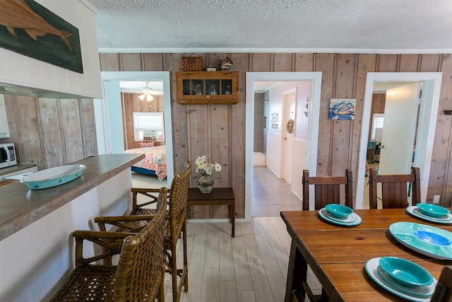 dining space with a textured ceiling, ceiling fan, wooden walls, and light wood-type flooring