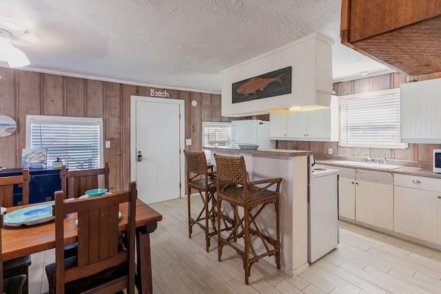 kitchen with white cabinetry, sink, a textured ceiling, wooden walls, and white appliances